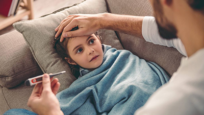 sick-young-girl-lying-on-a-couch-with-her-father-sitting-next-to-her-holding-a-thermometer-and-feeling-her-forehead