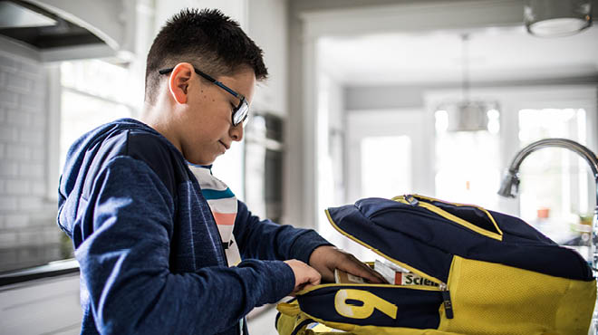 Child putting school supplies in backpack