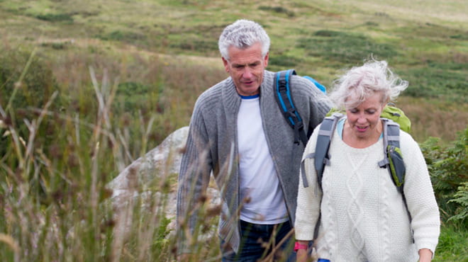 Middle-age couple hiking up hill wearing backpacks