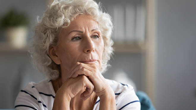 Person with grey hair, hands cupped on chin