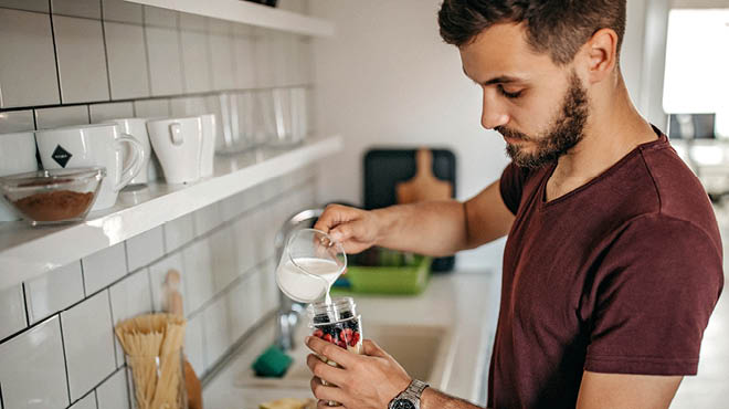 At kitchen counter, pouring milk into cup with fruit