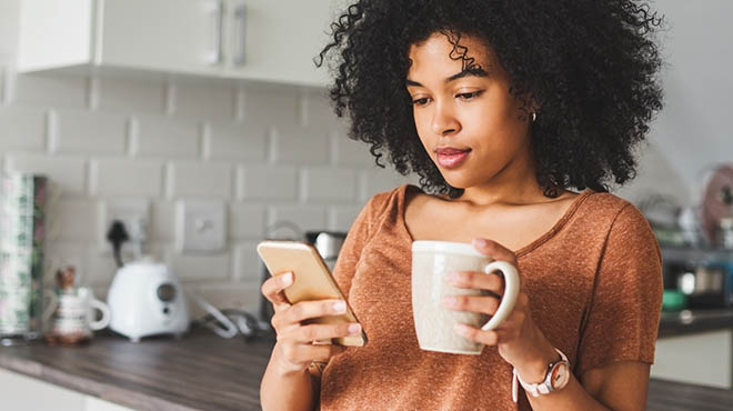 Holding mug and looking at cellphone while in the kitchen