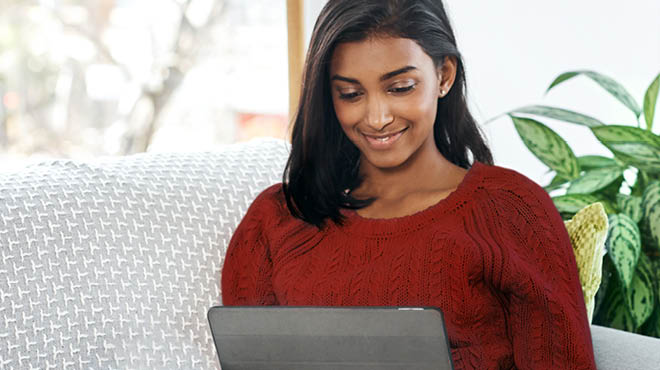 Sitting on sofa, looking at screen, wearing a cranberry-colored sweater