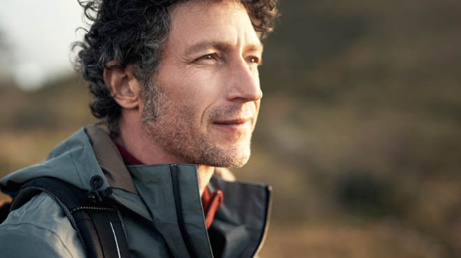 Middle-aged person with curly hair and grey beard stubble