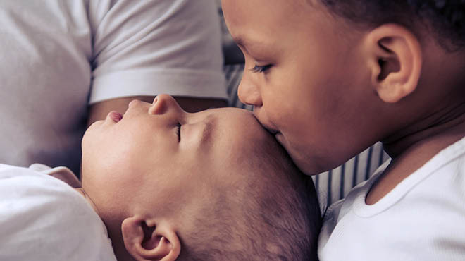 Toddler kissing head of baby