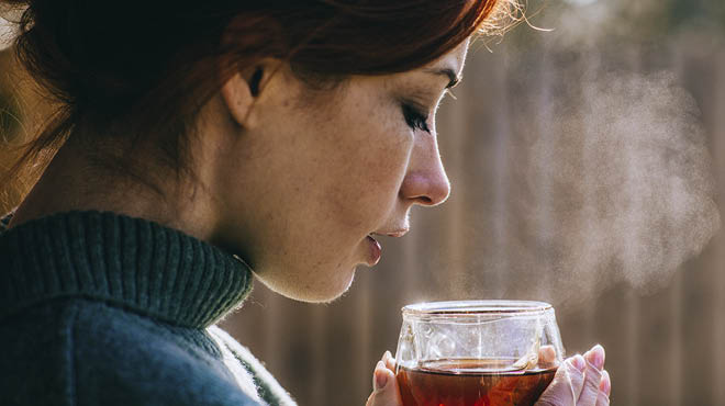 Person holding a clear mug with dark beverage inside and steam coming out. 